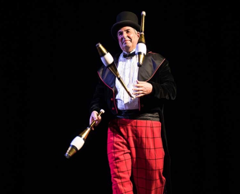 photo of a juggler performing with three clubs on stage