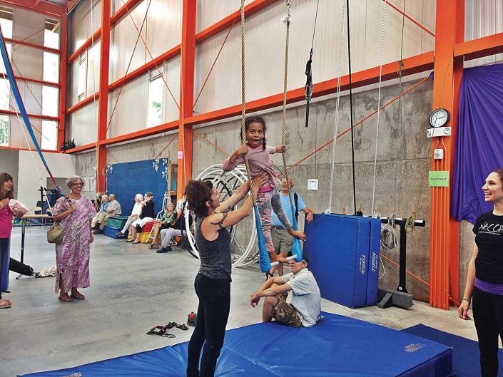 necca-shows-off-new-home-FEAT young child on a trapeze with the help of a NECCA coach